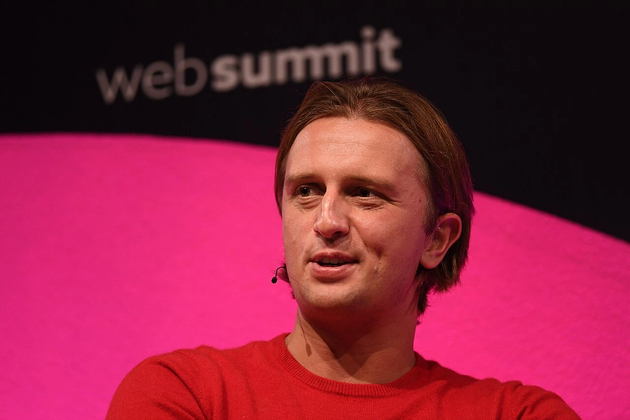 Nikolay Storonsky speaking on stage at Web Summit, wearing a red sweater against a pink background.