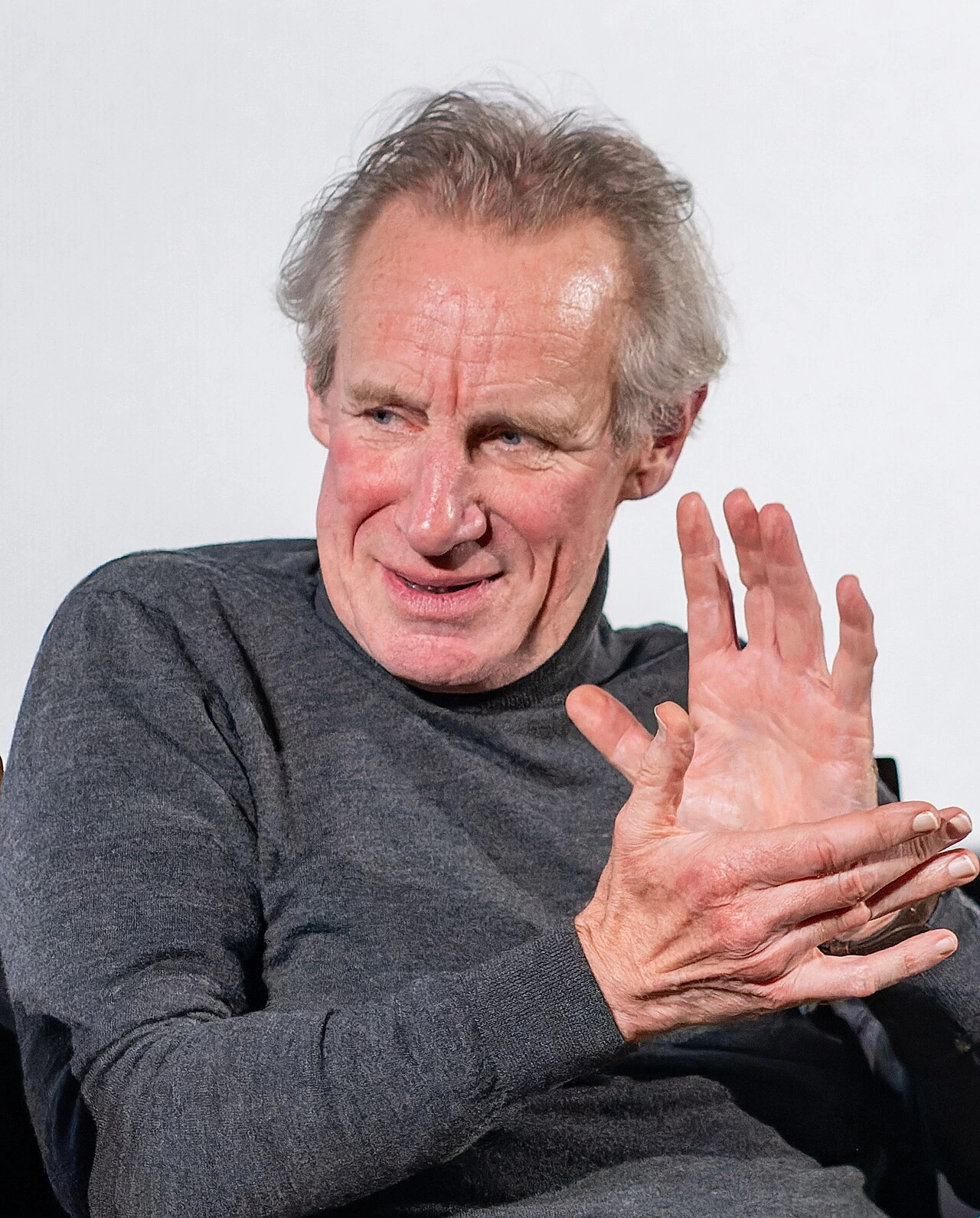 Nicholas Farrell at an event, seated and gesturing during a talk.