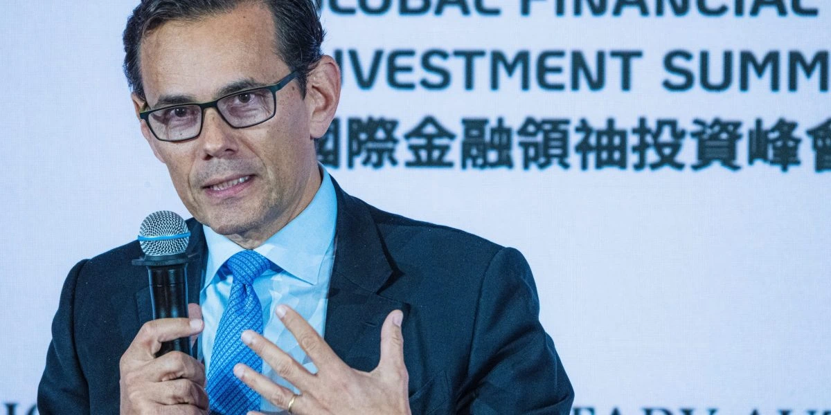 A man in a suit and tie speaking into a microphone at a financial investment summit.