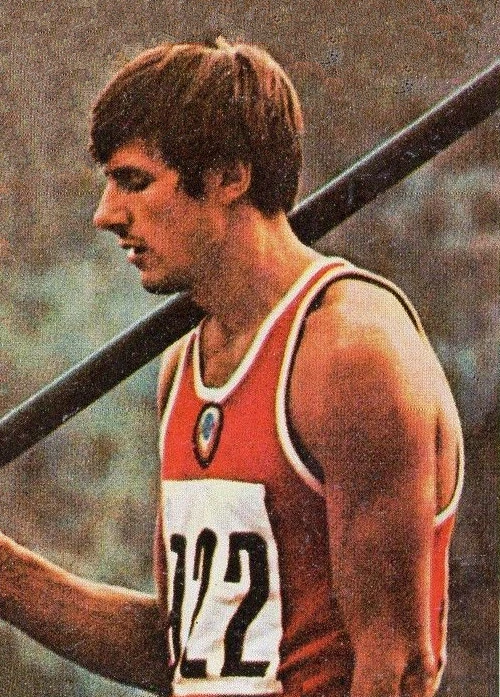 Nikolái Avilov in a track and field competition, shown in profile wearing a red athletic singlet with bib number 722
